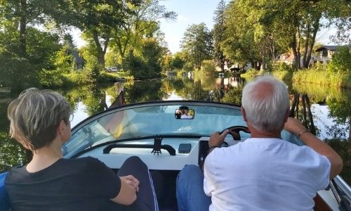 Ein Mann und eine Frau sitzen in einem Boot, man sieht sie von hinten, wie sie auf einem Kanal fahren.