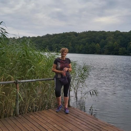 Eine Frau in sportlicher Kleidung steht auf einem Steg an einem See